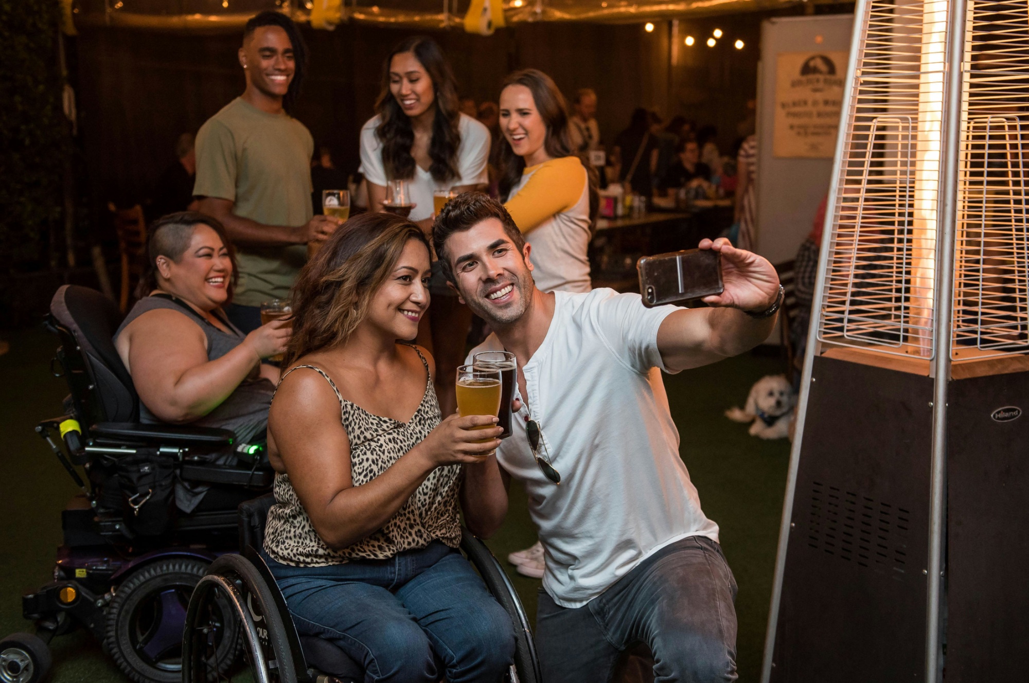 A diverse group of friends celebrating at a bar, including people using wheelchairs, laughing together