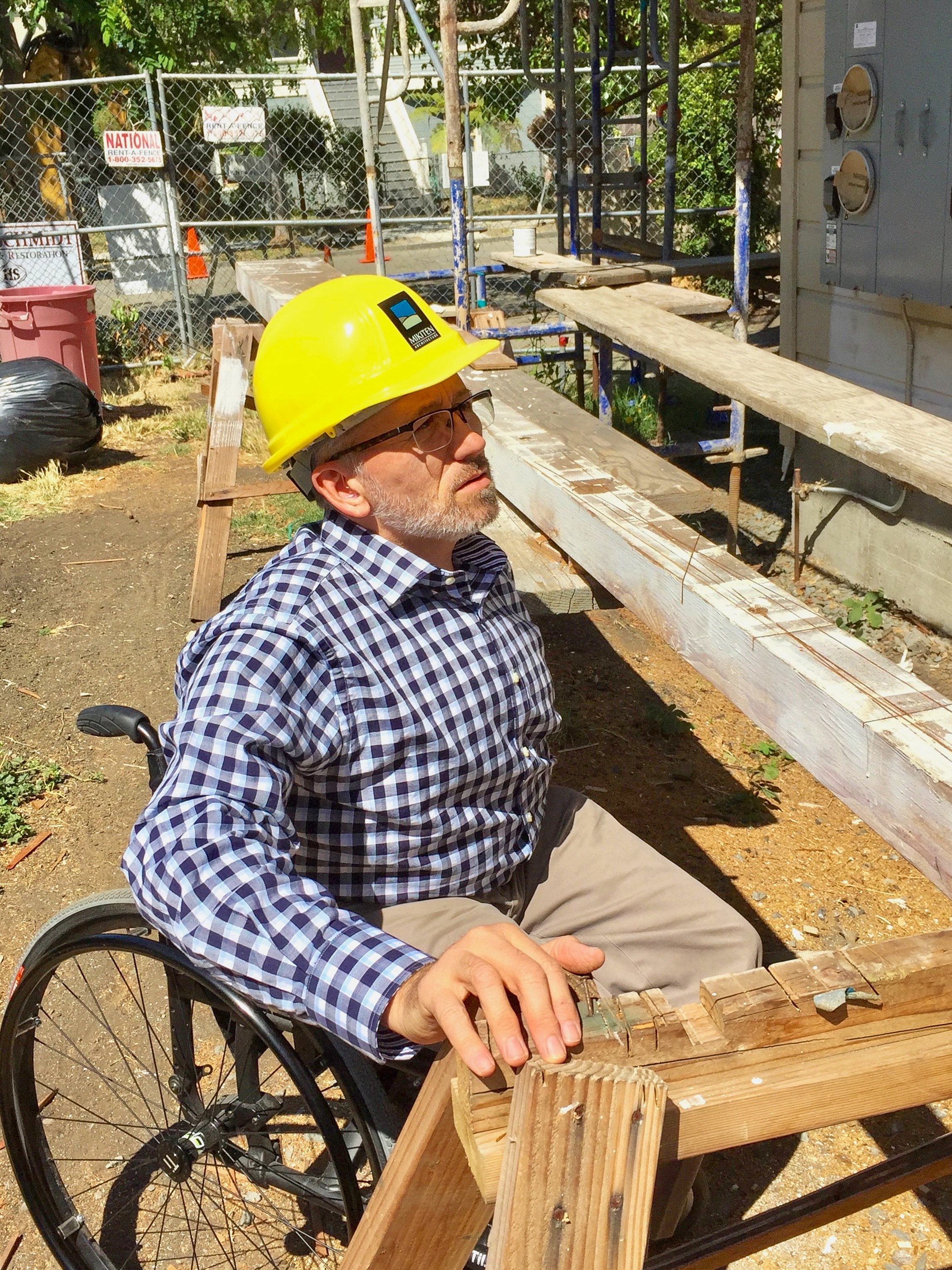 Erick in a yellow hardhat at a construction site, looking up at the framing