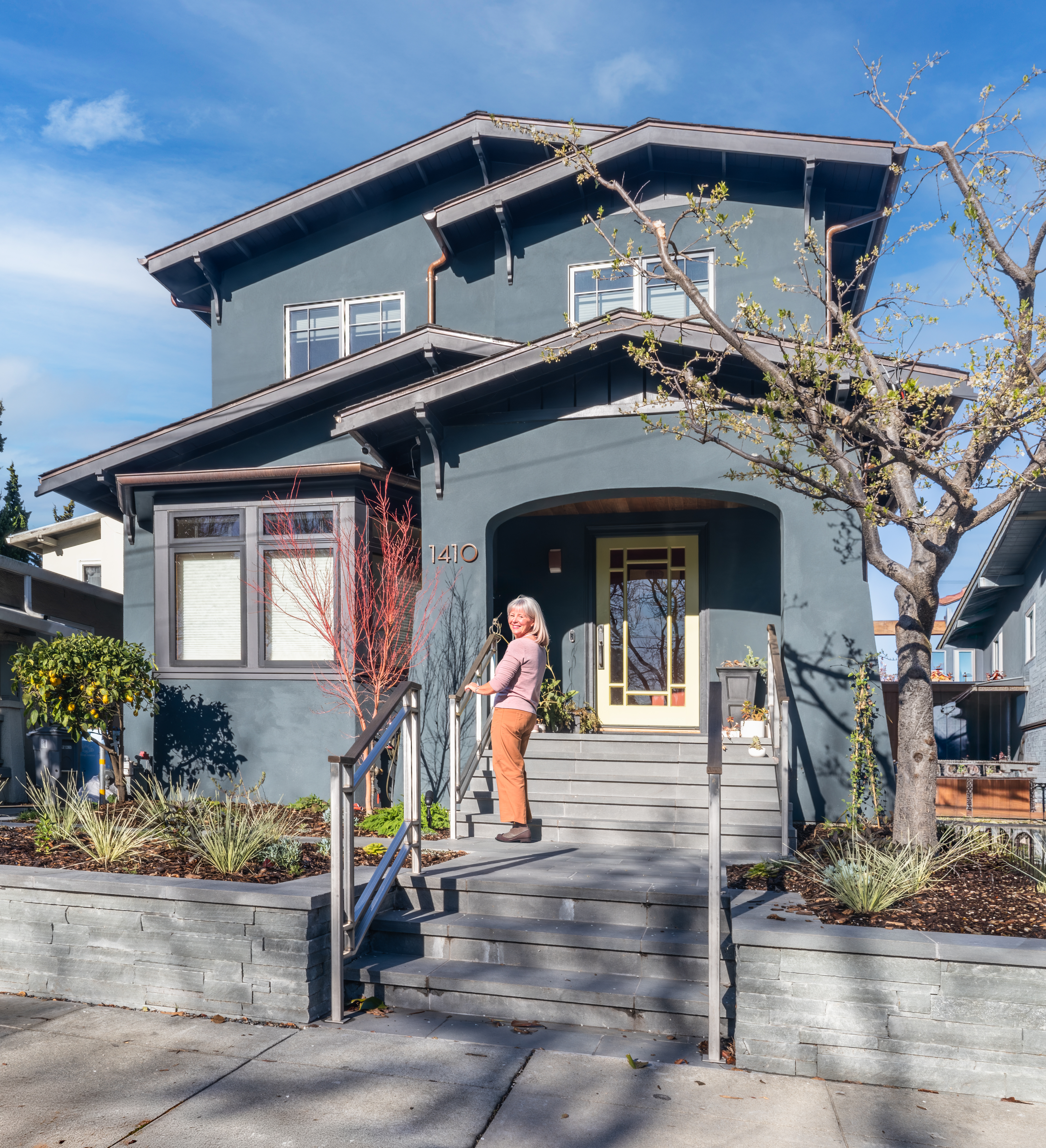 A woman smiling as she uses a handrail to walk up the front steps of a beautiful craftsman home